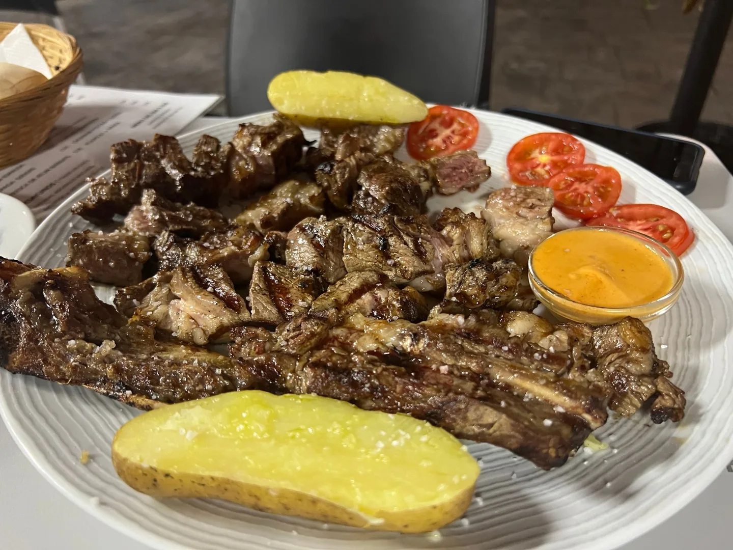 Platter of grilled meat, potatoes, and tomatoes