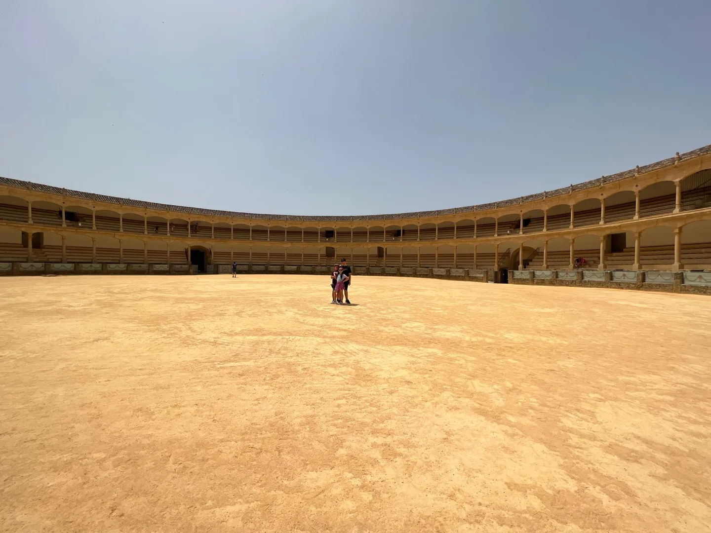 Empty sandy bullring surrounded by arcades