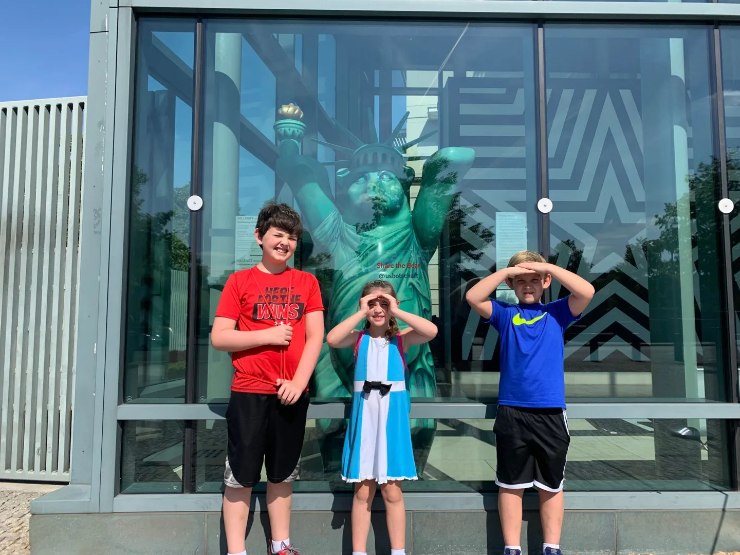 Children posing beside a green bear statue