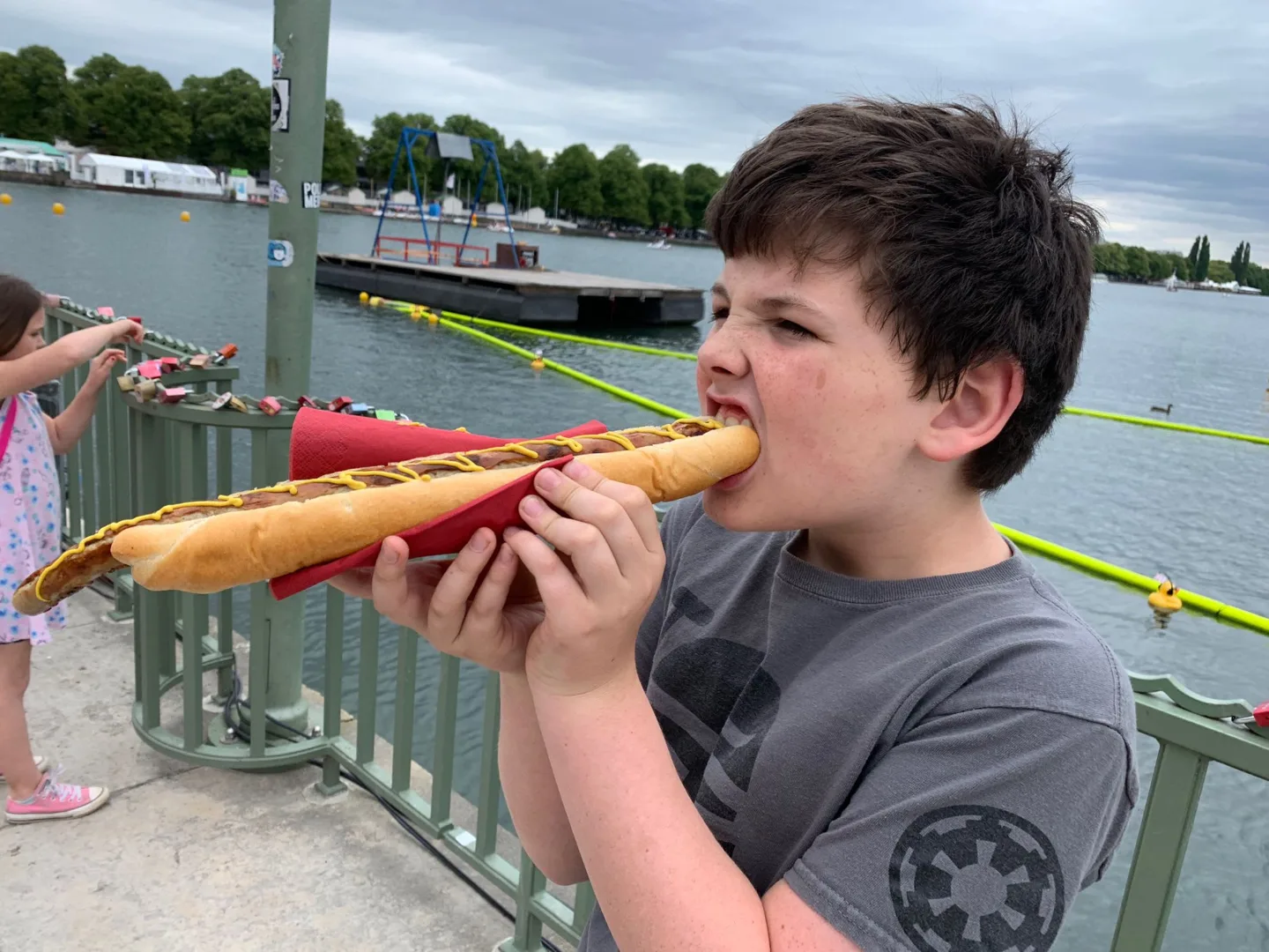 Child eating a long sandwich by the water