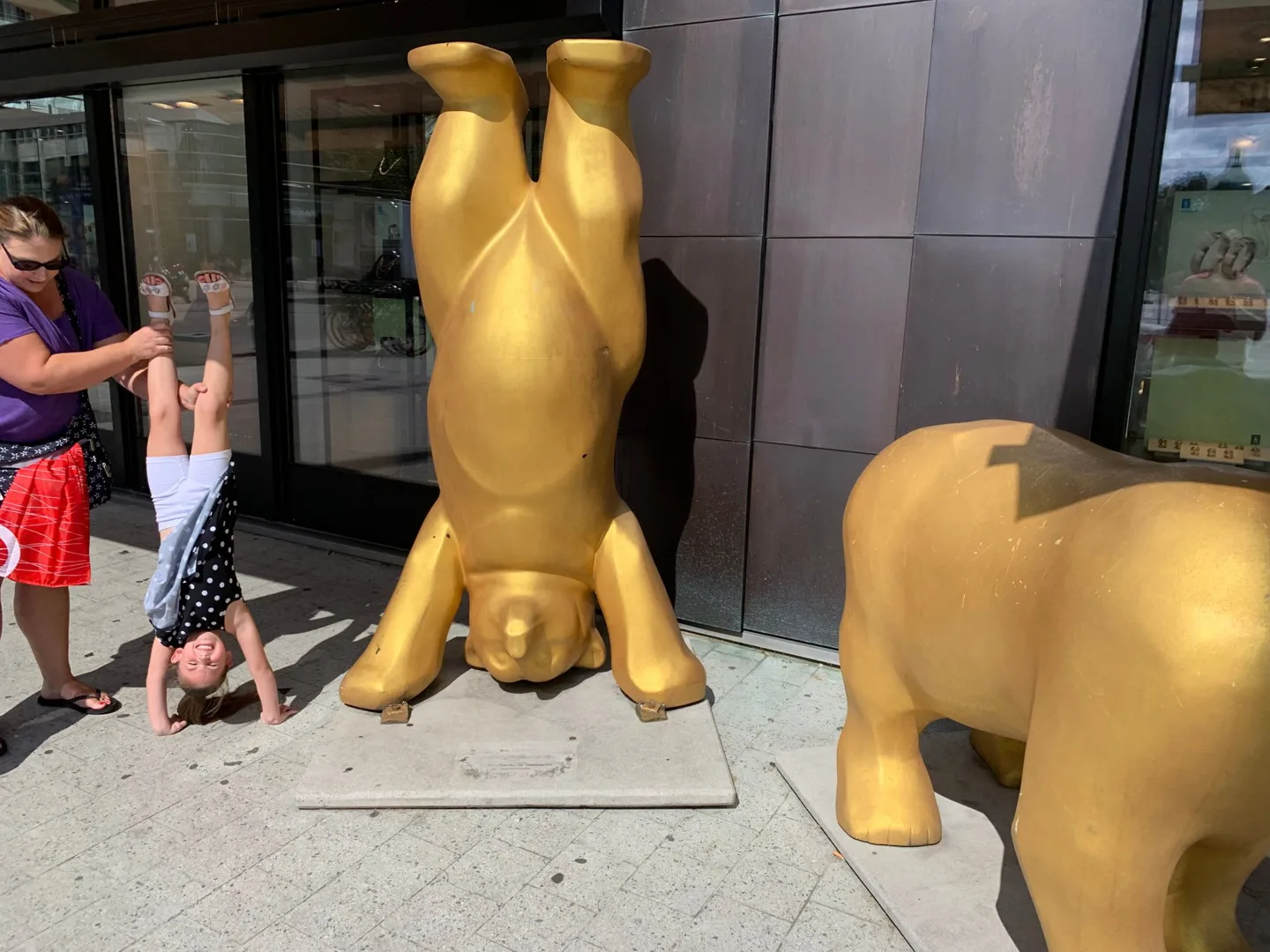 Child beside upside-down golden bear sculptures