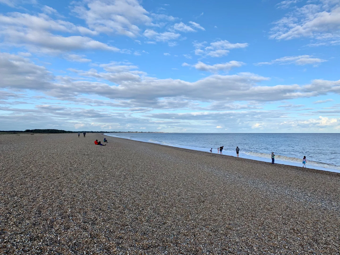 People walking along a broad pebble beach